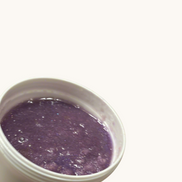Creation Essential's Natural Body Sweet Kisses shimmer body scrub in a white jar with a purple exfoliating texture.
