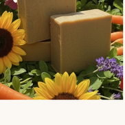 Creation Essential's Natural Body Carrot Delight bar soap nestled among fresh carrots, sunflowers, and hydrangeas.