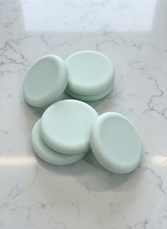 Five light green round soap bars textured brown surface