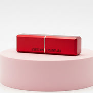 Red lipstick on a pink cylindrical stand with 'CREME ESSENTIALS' branding on a white background