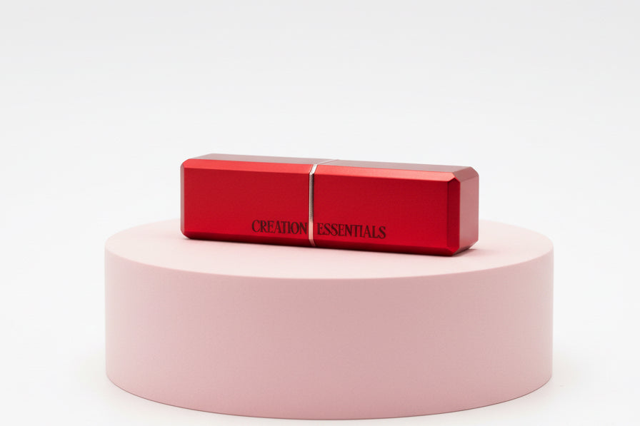 Red lipstick on a pink cylindrical stand with 'CREME ESSENTIALS' branding on a white background