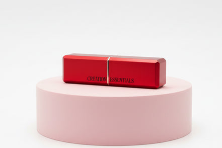 Red lipstick on a pink cylindrical stand with 'CREME ESSENTIALS' branding on a white background
