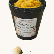 Creation Essential's Natural Body Revive creamy sugar scrub with turmeric and oats in a black jar on marble surface
