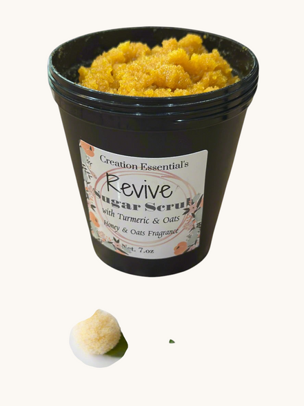 Creation Essential's Natural Body Revive creamy sugar scrub with turmeric and oats in a black jar on marble surface