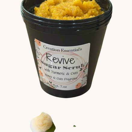 Creation Essential's Natural Body Revive creamy sugar scrub with turmeric and oats in a black jar on marble surface