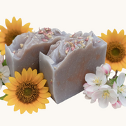 Creation Essential's Natural Body Honey Harvest soap bar topped with dried flowers, surrounded by sunflowers and apple blossoms.