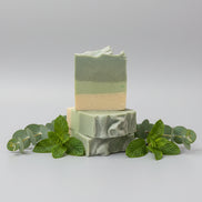 Two stacked green soap bars on a textured surface with a blurred background