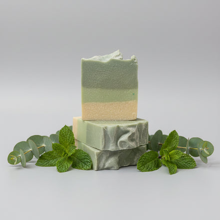 Two stacked green soap bars on a textured surface with a blurred background
