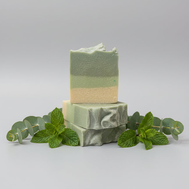 Two stacked green soap bars on a textured surface with a blurred background