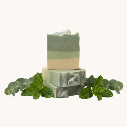 Two stacked green soap bars on a textured surface with a blurred background