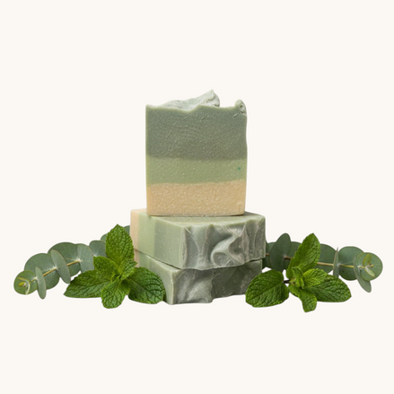 Two stacked green soap bars on a textured surface with a blurred background