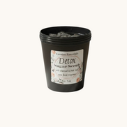 Creation Essential's Natural Body charcoal and pink salt detox body mask scrub in a black jar on a marble pedestal.