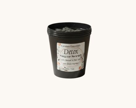 Creation Essential's Natural Body charcoal and pink salt detox body mask scrub in a black jar on a marble pedestal.