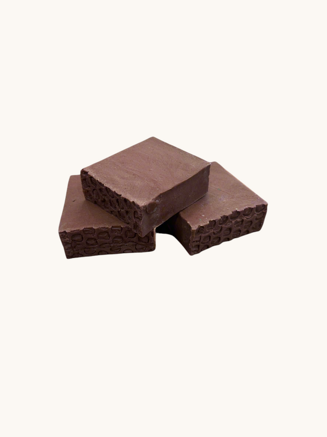 Creation Essential's Natural Body Sweet Harvest bar soap with red clay and textured edges on a marble surface.