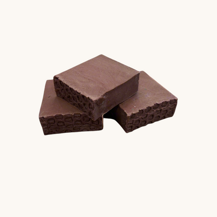 Creation Essential's Natural Body Sweet Harvest bar soap with red clay and textured edges on a marble surface.