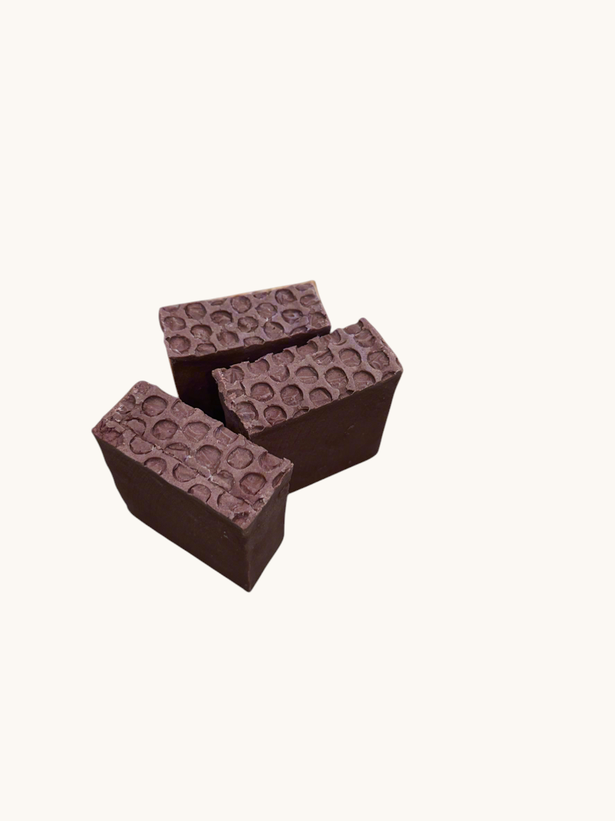 Creation Essential's Natural Body Sweet Harvest bar soap with a textured honeycomb top on a tropical leaf background.