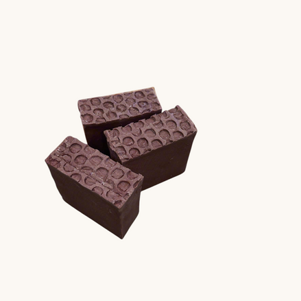 Creation Essential's Natural Body Sweet Harvest bar soap with a textured honeycomb top on a tropical leaf background.