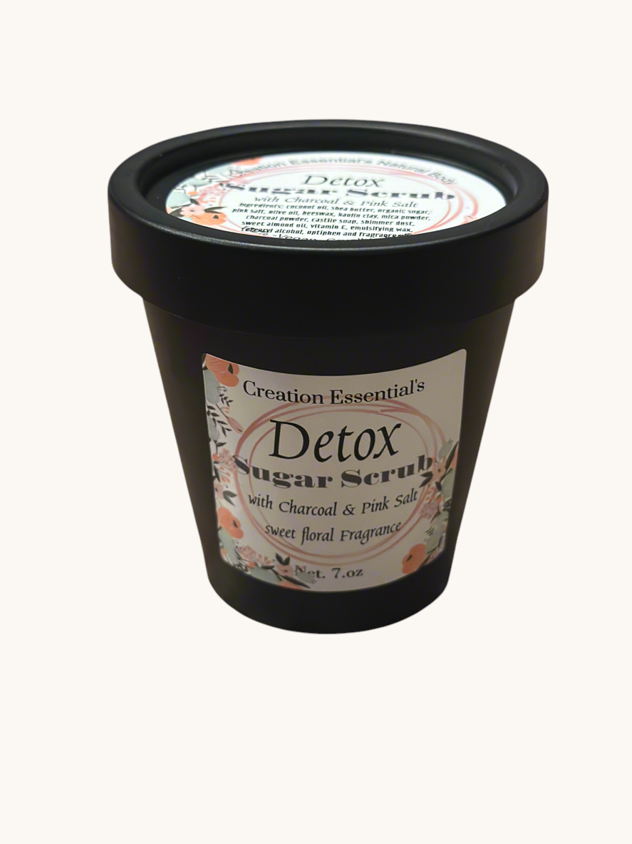 Creation Essential's Natural Body Detox Sugar Scrub in a black jar with floral label on a white marble surface