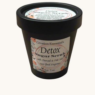Creation Essential's Natural Body Detox Sugar Scrub in a black jar with floral label on a white marble surface