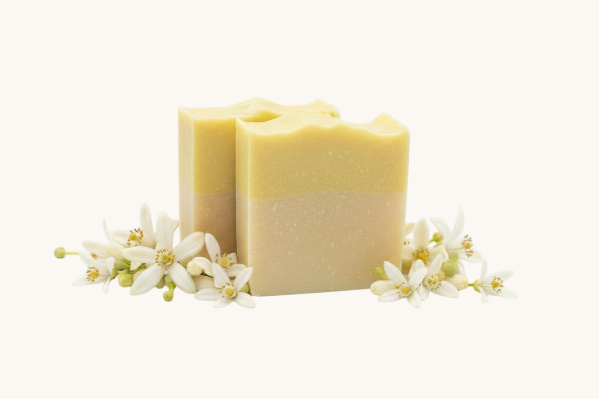 Creation Essential's Natural Body citrus bar soap with raw honey and aloe vera, surrounded by fresh white blossoms.