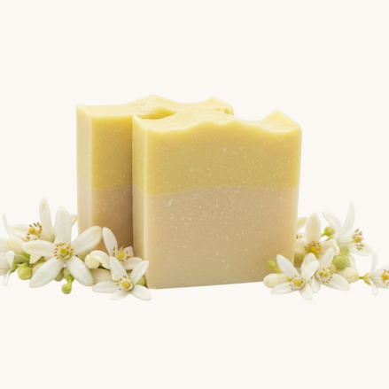 Creation Essential's Natural Body citrus bar soap with raw honey and aloe vera, surrounded by fresh white blossoms.