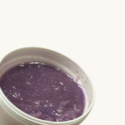 Hand holding a white container with purple Sugar Scrub