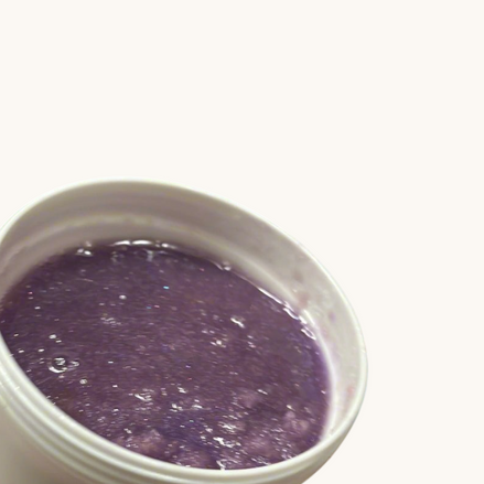 Hand holding a white container with purple Sugar Scrub