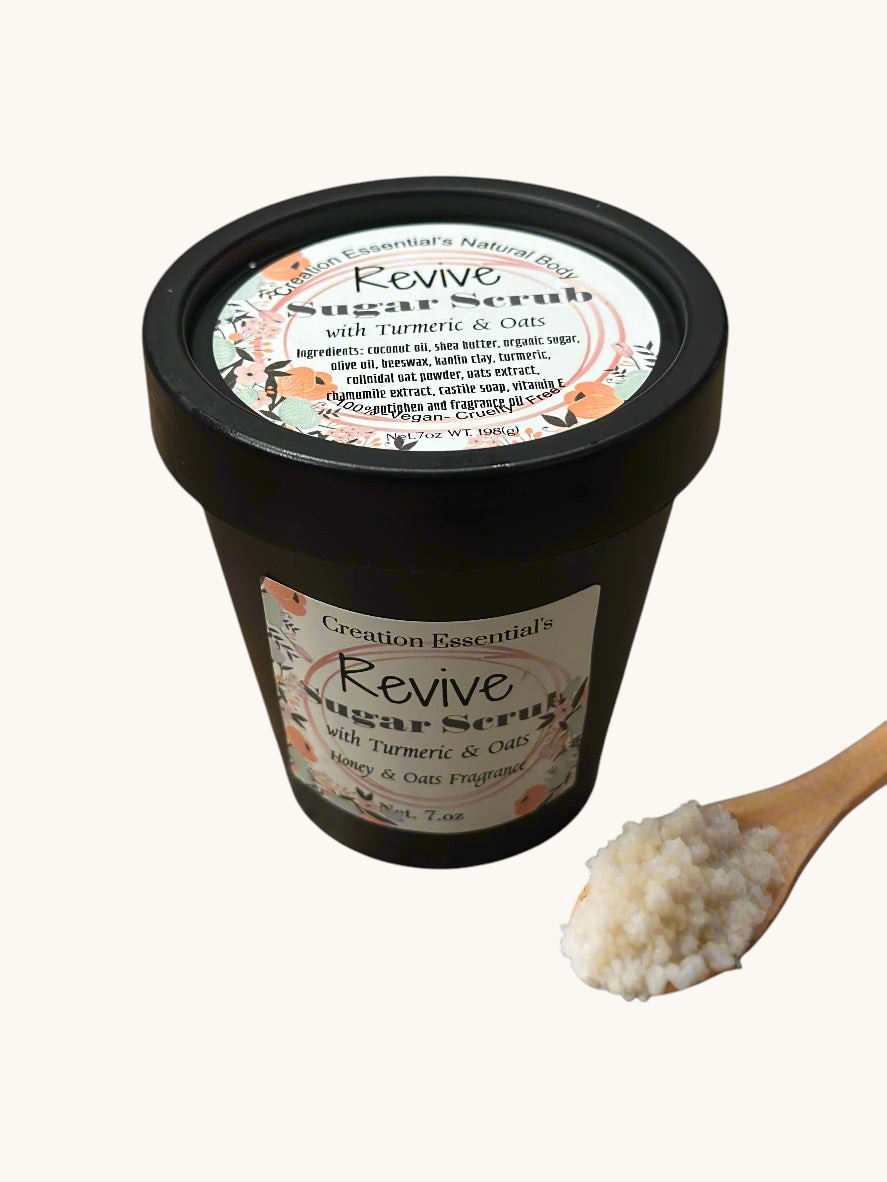 Creation Essential's Natural Body Revive creamy sugar scrub with turmeric and oats in a black jar with a wooden spoon.