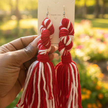 A pair of handcrafted yarn earrings with a twisted knot design, featuring colors green, red, and white, displayed on a card.