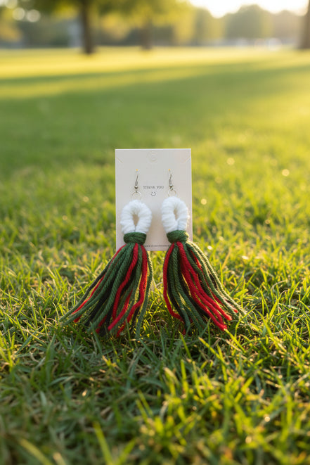 A pair of handcrafted yarn earrings with a twisted knot design, featuring colors green, red, and white, displayed on a card.