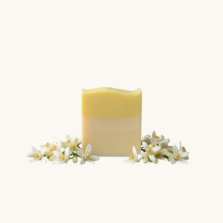 Creation Essential's Natural Body citrus bar soap with raw honey and aloe vera, surrounded by fresh white blossoms.