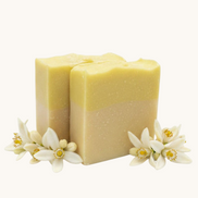 Creation Essential's Natural Body citrus bar soap with raw honey and aloe vera, decorated with fresh white blossoms.