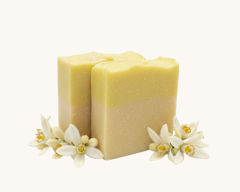Creation Essential's Natural Body citrus bar soap with raw honey and aloe vera, decorated with fresh white blossoms.