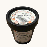 Creation Essential's Natural Body detox sugar scrub with charcoal and pink salt in a black jar on a marble surface.