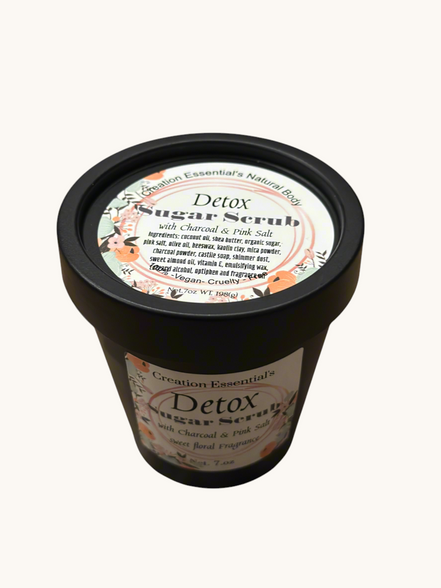 Creation Essential's Natural Body detox sugar scrub with charcoal and pink salt in a black jar on a marble surface.