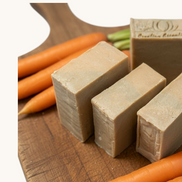 Creation Essential's Natural Body Carrot Delight bar soap on a wooden board with fresh carrots