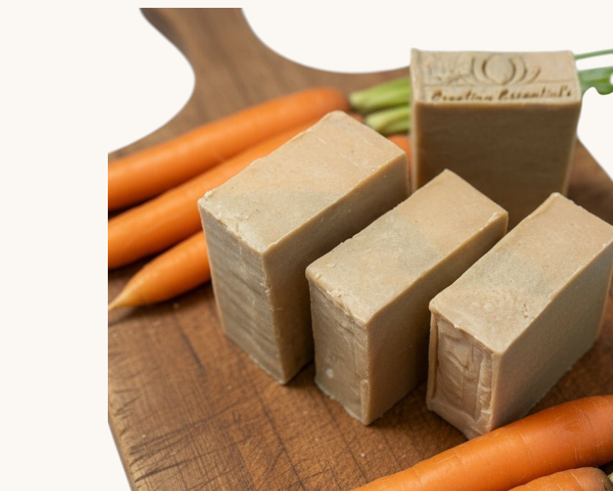 Creation Essential's Natural Body Carrot Delight bar soap on a wooden board with fresh carrots