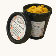 Creation Essential's Natural Body Revive creamy sugar scrub with turmeric and oats in a black jar on a wooden table.