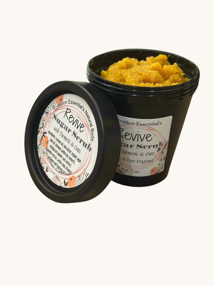 Creation Essential's Natural Body Revive creamy sugar scrub with turmeric and oats in a black jar on a wooden table.