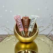 Three Allure lip gloss tubes on a gold surface
