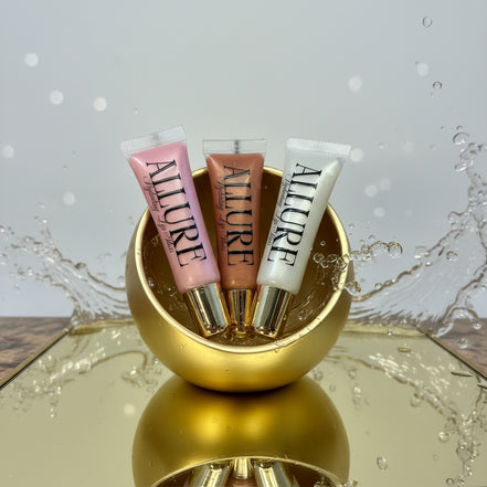 Three Allure lip gloss tubes on a gold surface