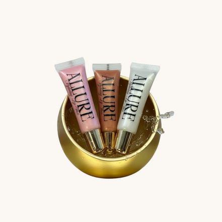Three Allure lip gloss tubes on a gold surface