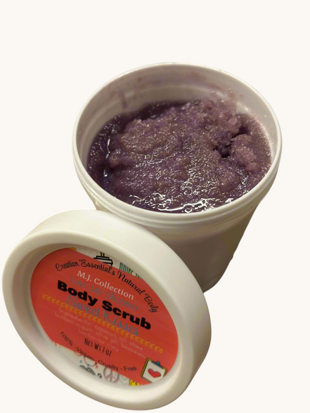 Two containers of body scrub with a purple scrub and visible label on a gray surface with green leaves.