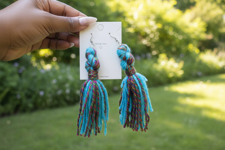 A pair of handcrafted yarn earrings with a twisted knot design, featuring colors green, red, and white, displayed on a card.